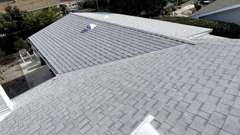 Elevated view of a light-gray asphalt shingle roof on a single-story house showing hips, a long ridge and a valley across most of the frame.